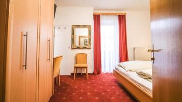 Une chambre d’hôtel avec un lit, une chaise, une armoire, un miroir et une fenêtre avec des rideaux.