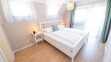 Un dormitorio con cama blanca, mesitas de noche y lámpara colgante.