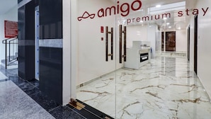 Een moderne hotellobby met een marmeren vloer, glazen deuren en een bord met de tekst 'amigo premium stay'.