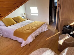 Ein Schlafzimmer mit einem Bett, einem Nachttisch, einer Lampe, einem Koffer und einem Korbsessel.
