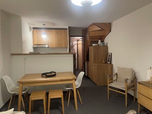 A compact living space with a kitchenette, a dining area with a wooden table and chairs, and a small seating area with a chair and a side table. - Apartment in Serre Chevalier, near the slopes - 3 bedrooms - sleeps 6 (Le Monêtier-les-Bains)