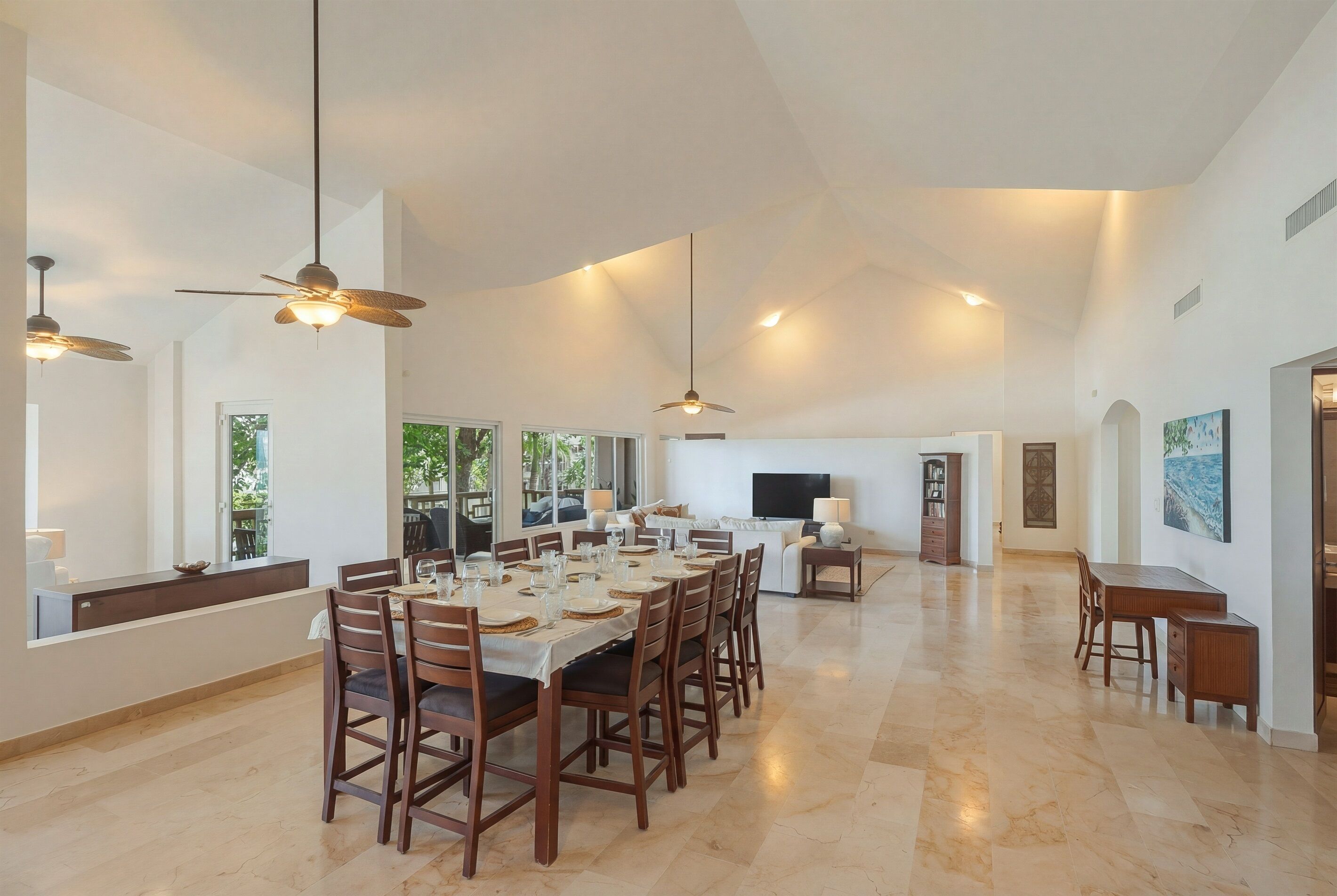 A spacious dining area with a long table, multiple chairs, ceiling fans, and a television.