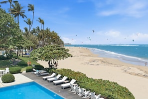 A poolside area with lounge chairs, a swimming pool, and a beach with people and kites. - Ocean Front Penthouse 4BR/4B (Kite Beach)