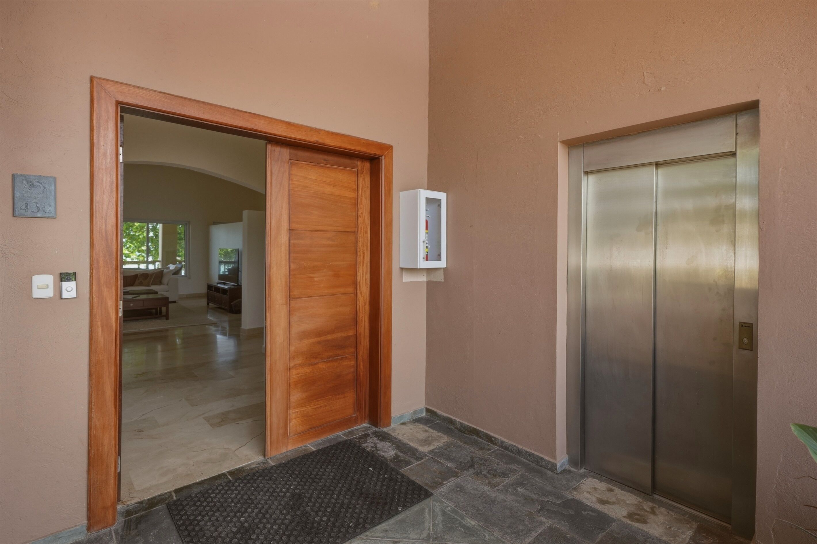 A hallway with a wooden door, an elevator, and a thermostat on the wall.