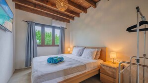 Ein Schlafzimmer mit einem Bett, einem Nachttisch, einer Lampe, einem Fenster mit Vorhängen und einem Deckenventilator.