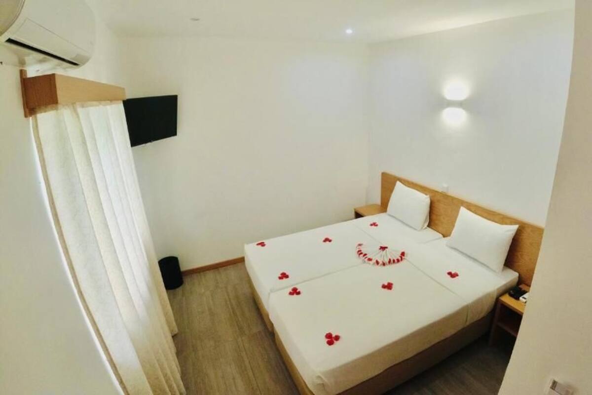 A hotel room with a bed, a TV mounted on the wall, and a wooden headboard.