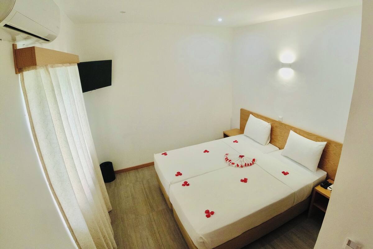 A hotel room with a bed, a bedside table, a wall-mounted TV, and a ceiling-mounted air conditioner.