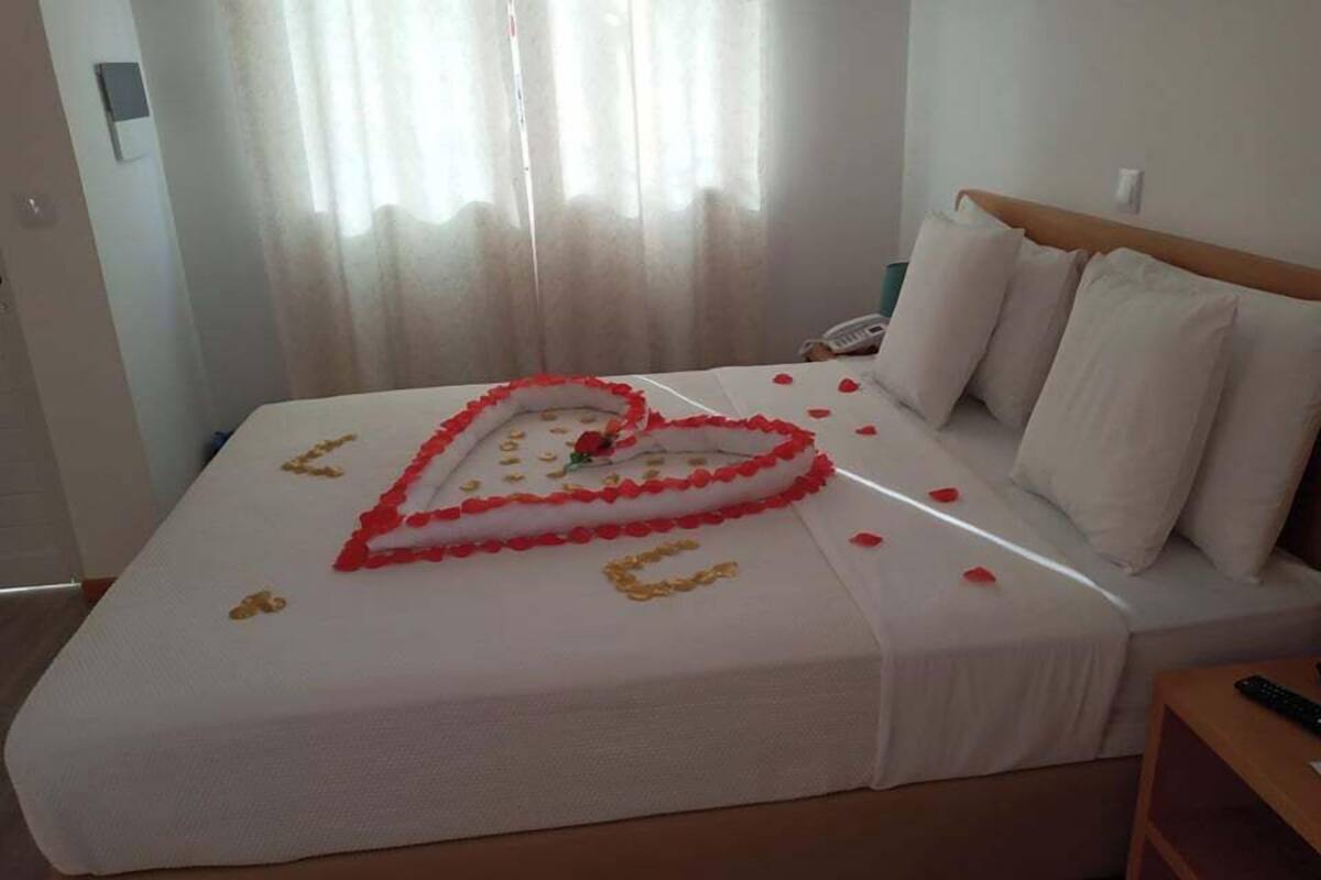 A hotel room with a bed, a bedside table, and a window with curtains.