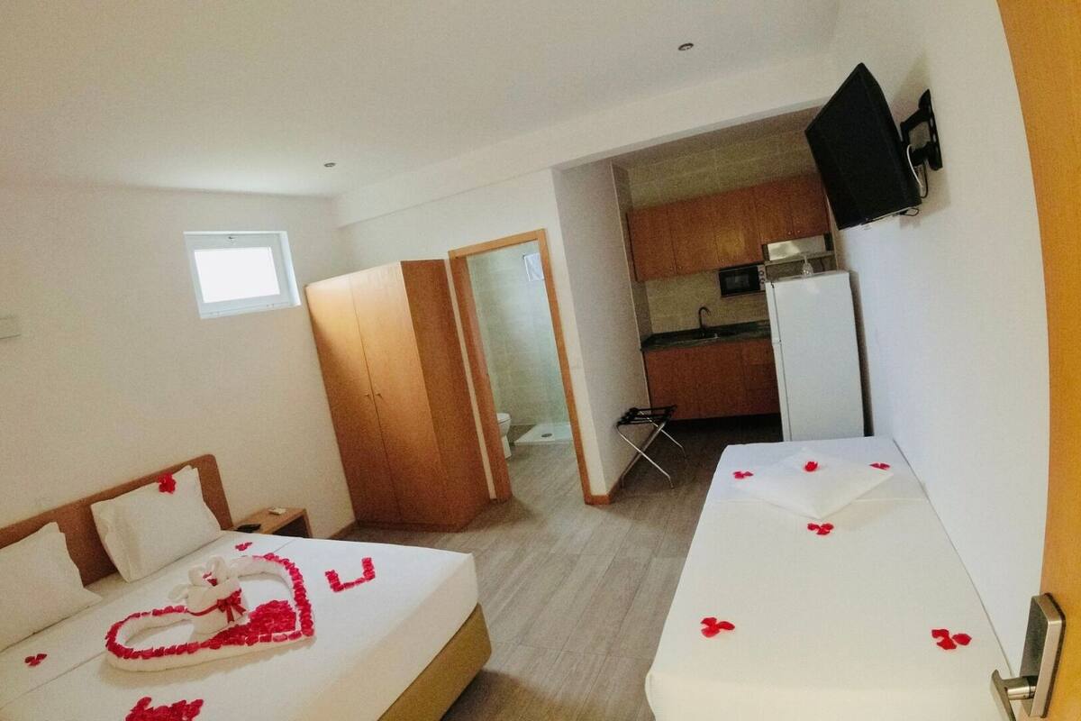 A hotel room with two beds, a kitchenette, and a bathroom visible through an open door.