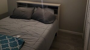 A bedroom with a bed, pillows, a bedside table, and a wall-mounted light fixture. - 2-bedroom condo in gorgeous Calabash with cool AC breeze (Calabash)