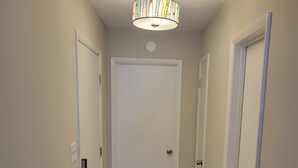 A hallway with a wooden floor, white doors, and a ceiling light fixture. - 2-bedroom condo in gorgeous Calabash with cool AC breeze (Calabash)