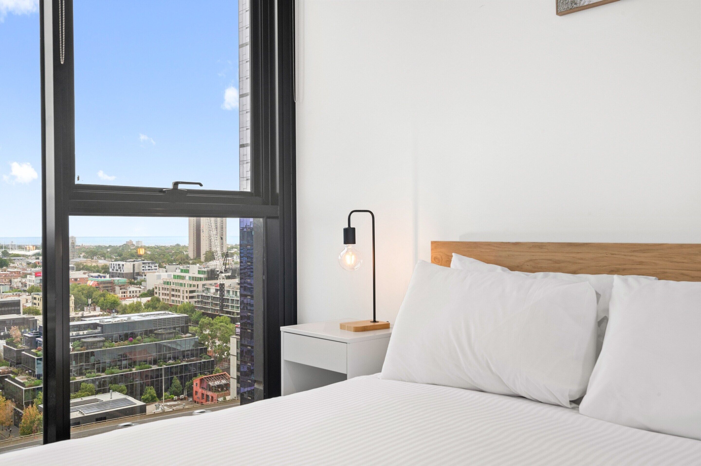 A hotel room with a large window, a bed, a nightstand, and a lamp.