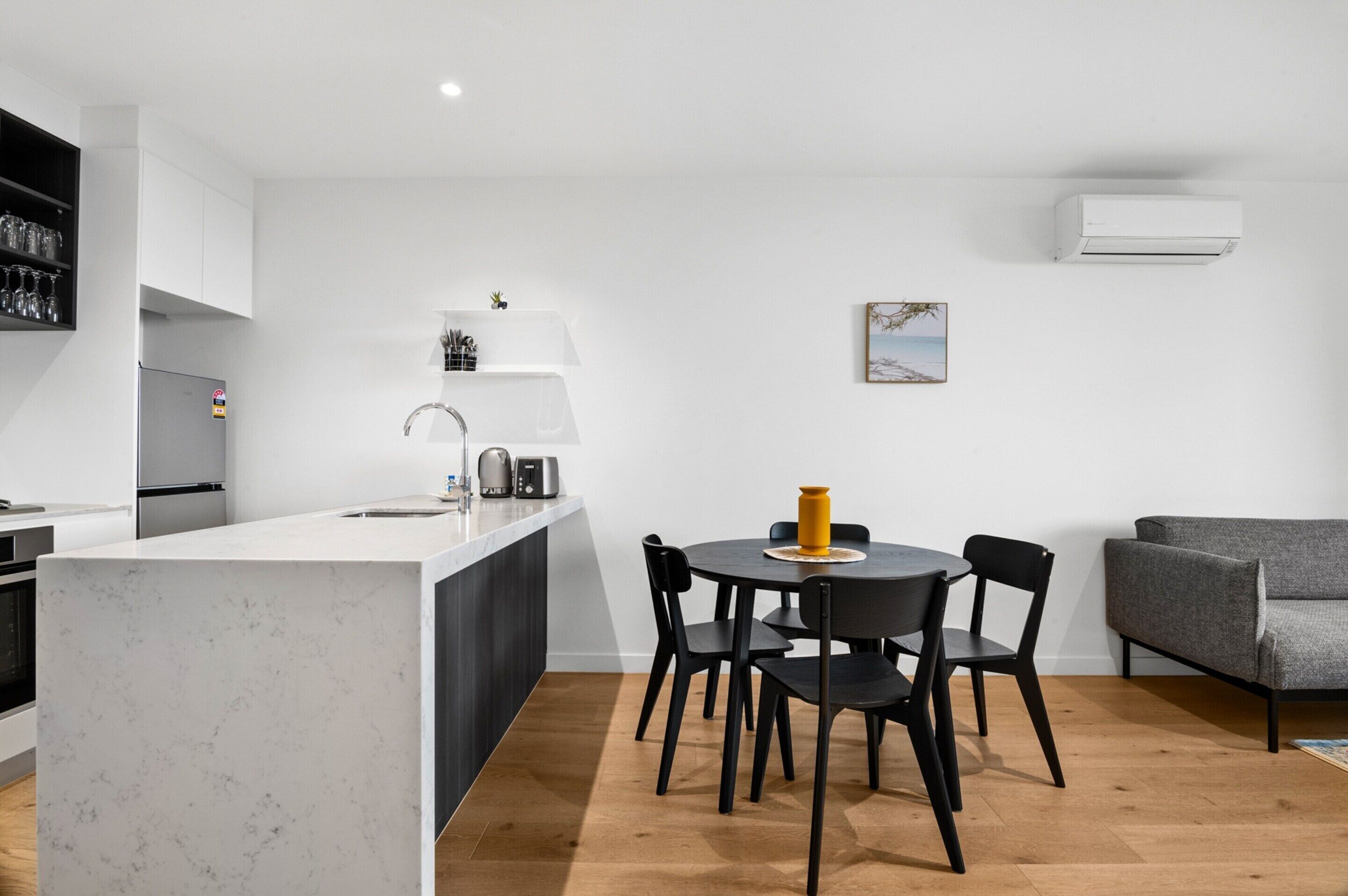 Une cuisine moderne avec un îlot central, un coin repas avec une table ronde et des chaises, et un canapé gris.