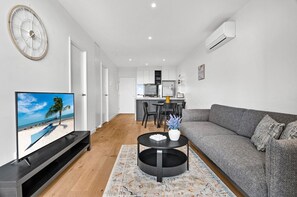 A modern living room with a flat-screen TV, a gray sofa, a coffee table, and a kitchen in the background. - Central Southbank Apartment With Pool Access (Melbourne)