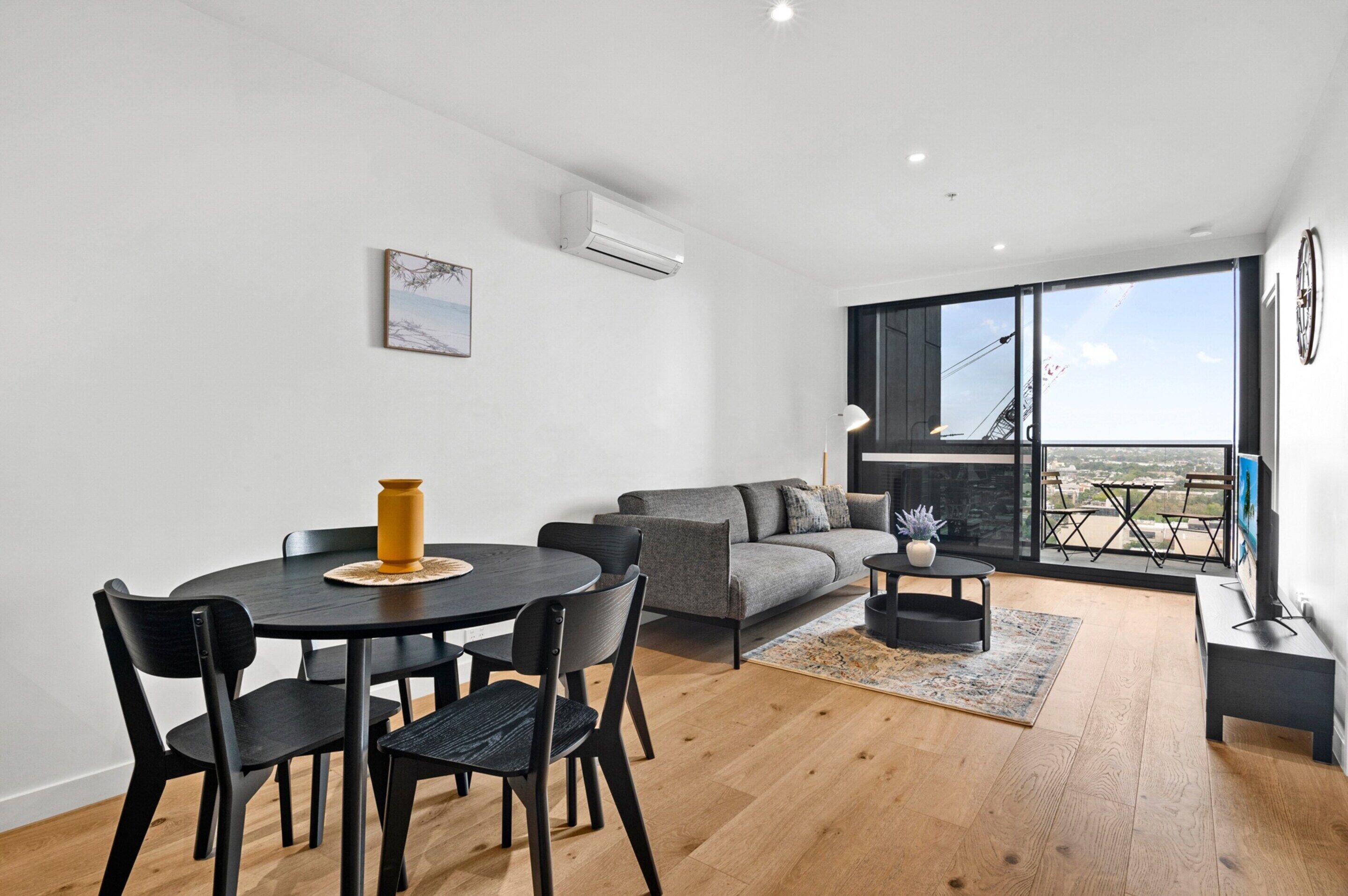 A modern living room with a dining table, chairs, a sofa, and a large window with a view.