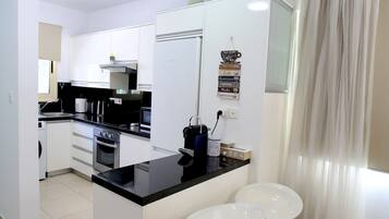 A modern kitchen with white cabinets, a black countertop, stainless steel appliances, and two white bar stools.