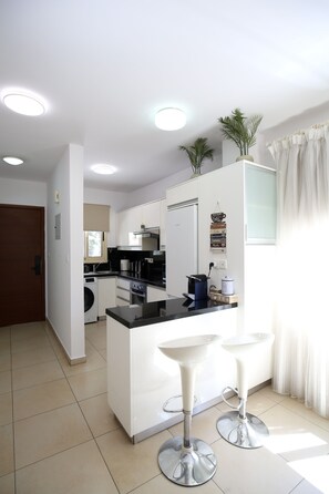 A modern kitchen with white cabinets, a central island, and two bar stools.