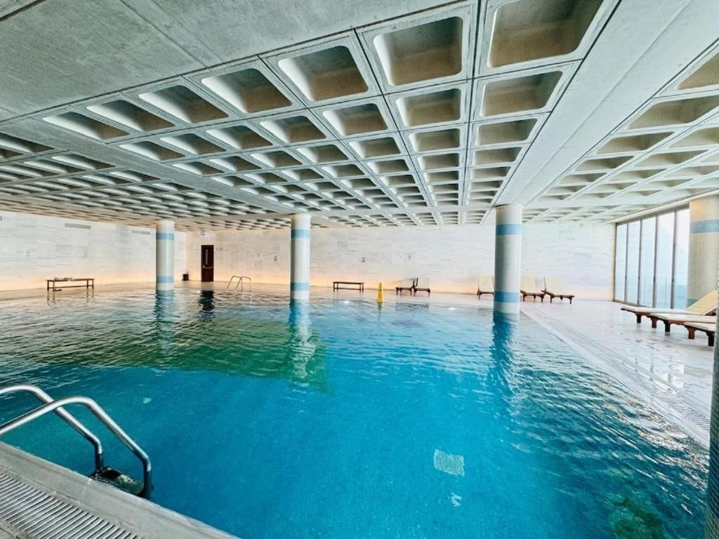 Una piscina interior con agua cristalina, una escalera de piscina y un techo con diseño de cuadrícula.