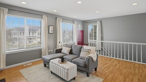 Una sala moderna con un sofá gris, un reposapiés y vistas al exterior.