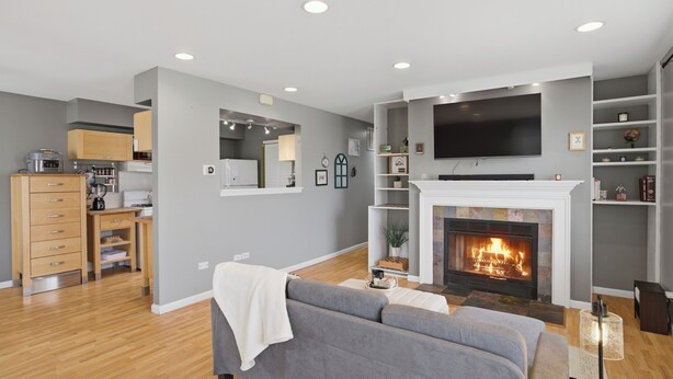 Una sala de estar moderna con chimenea, televisor de pantalla plana, sofá y una cocina al fondo.
