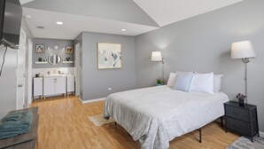 Un dormitorio con cama, mesitas de noche, televisor, escritorio y baño con espejo y lavamanos.