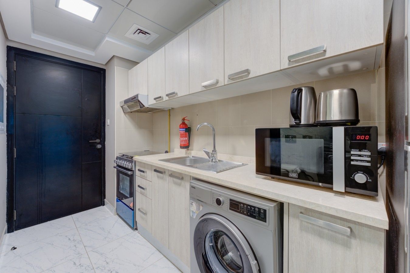 Une cuisine compacte équipée d’un lave-linge, d’un four à micro-ondes, d’un évier et d’une cuisinière.