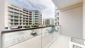 A modern apartment building with a glass balcony overlooking a parking area.