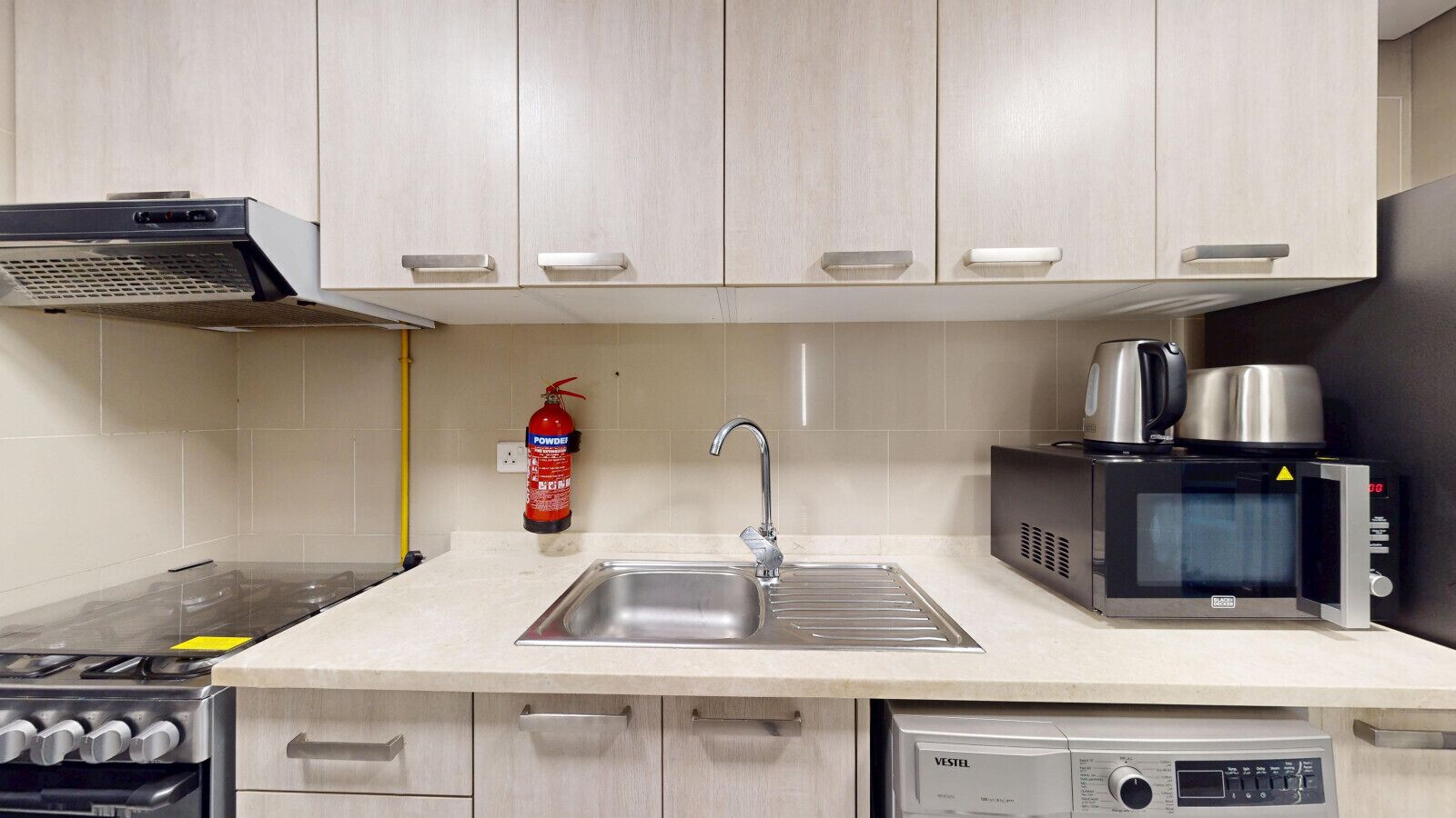Una cucina con lavandino in acciaio inossidabile, forno a microonde, macchina del caffè e estintore.