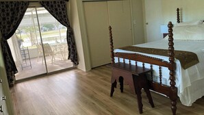 Ein Schlafzimmer mit einem hölzernen Bett, einem kleinen Tisch, einem Deckenventilator und einer Glastür, die zu einem Außenbereich führt.