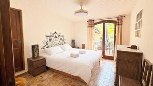A bedroom with a bed, a desk, a chair, a window with curtains, and a door. - The Olive Grove - Sea View (Saint-André-de-la-Roche)
