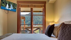 A hotel room with a bed, a view of a mountain, and a painting of sailboats. - Palisades View One Bedroom (Olympic Valley)