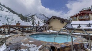 A pool area with stone flooring, a wooden fence, and a building with a sloped roof. - Palisades View One Bedroom (Olympic Valley)