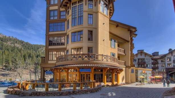 A multi-story building with a curved balcony, a restaurant on the ground floor, and a mountainous backdrop. - Palisades View One Bedroom (Olympic Valley)