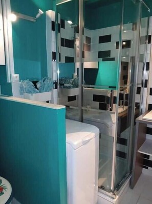 A modern bathroom with a glass shower enclosure, a white sink, and a teal accent wall. - Sea view studio with private parking & pool - All on foot 🌊 (Le Grau-du-Roi)