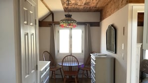 Une pièce avec un plafond en bois, une table à manger avec des chaises, une commode et une fenêtre avec des rideaux.