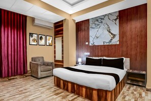 Une chambre d’hôtel avec un lit, une chaise, un bureau et un grand tableau abstrait accroché au mur.