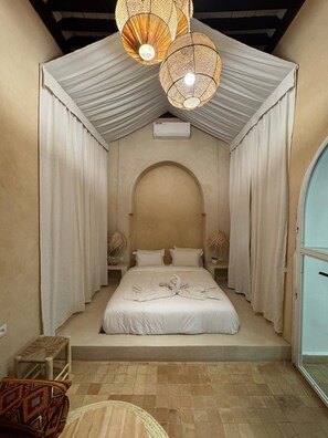 Un dormitorio con cama, cortinas, ventilador de techo y una pequeña mesa.