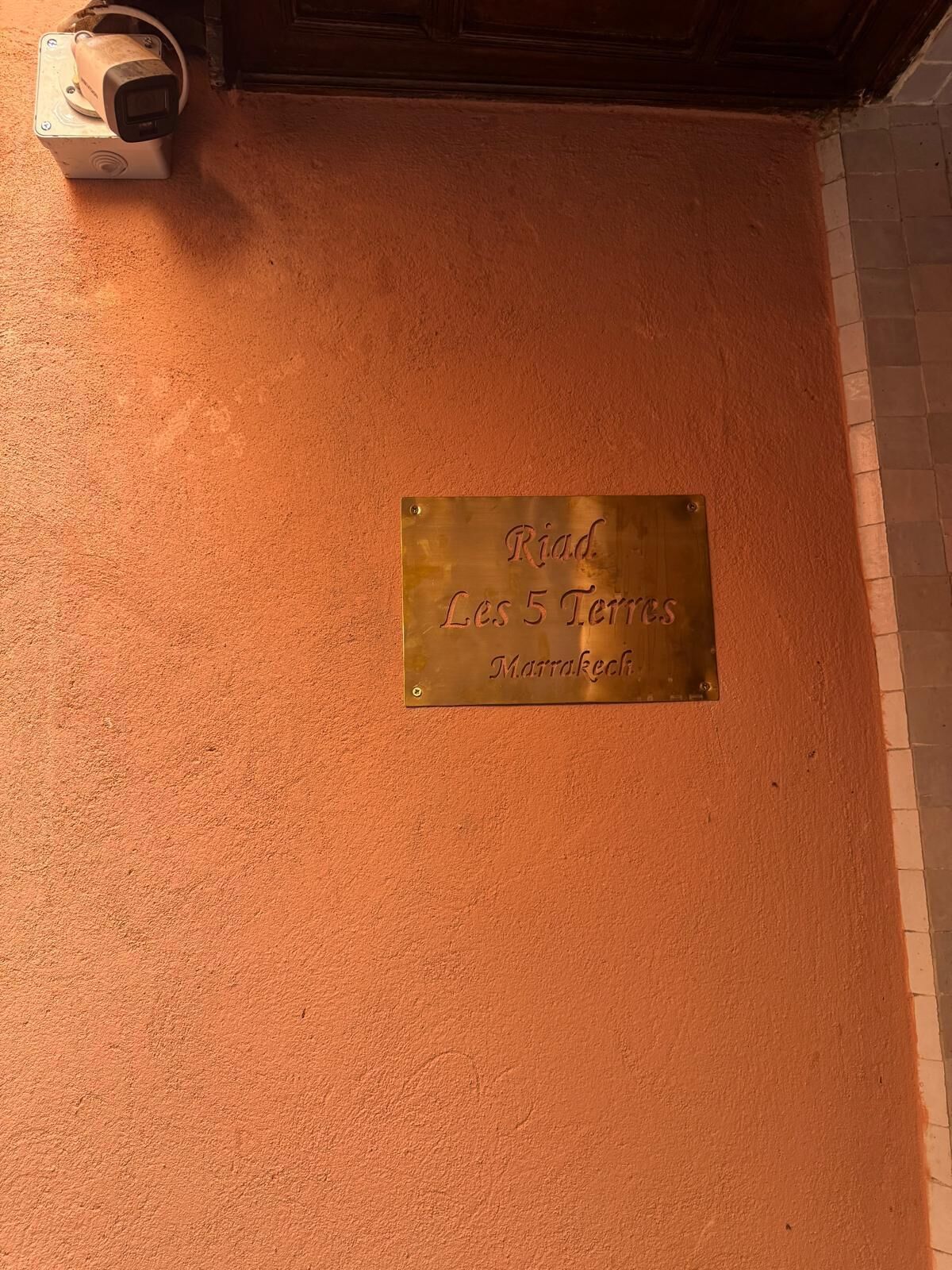 A plaque on a textured orange wall with the inscription 'Riad. Les 5 Terraces Marrakech.'