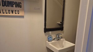 Ein Badezimmer mit Toilette, Waschbecken und Spiegel. Ein Schild an der Wand zeigt 'DUMPING ALLOWED'.