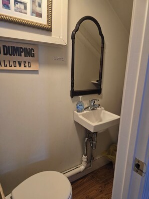 Ein Badezimmer mit Toilette, Waschbecken und Spiegel. Ein Schild an der Wand zeigt 'DUMPING ALLOWED'.