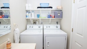 A laundry room with two front-loading washing machines, shelves above holding various laundry supplies, and a white towel hanging on a rack. - Keuka Lakeside Getaway (Penn Yan)