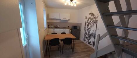 A compact kitchen with a dining table and chairs, a microwave, and a staircase.