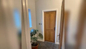 A hallway with a wooden door, a potted plant, and a carpeted floor. - The Snug - Newly Renovated Charming 1769 Cottage Escape in the Countryside. (Falfield)
