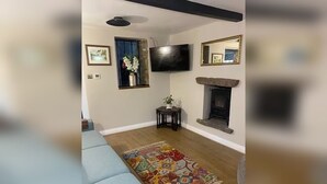 A living room with a blue sofa, a fireplace, a TV, and framed pictures on the wall. - The Snug - Newly Renovated Charming 1769 Cottage Escape in the Countryside. (Falfield)