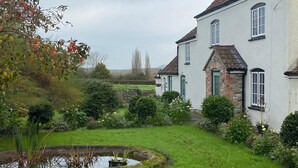 A traditional house with a garden, a pond, and a clear sky. - The Snug - Newly Renovated Charming 1769 Cottage Escape in the Countryside. (Falfield)