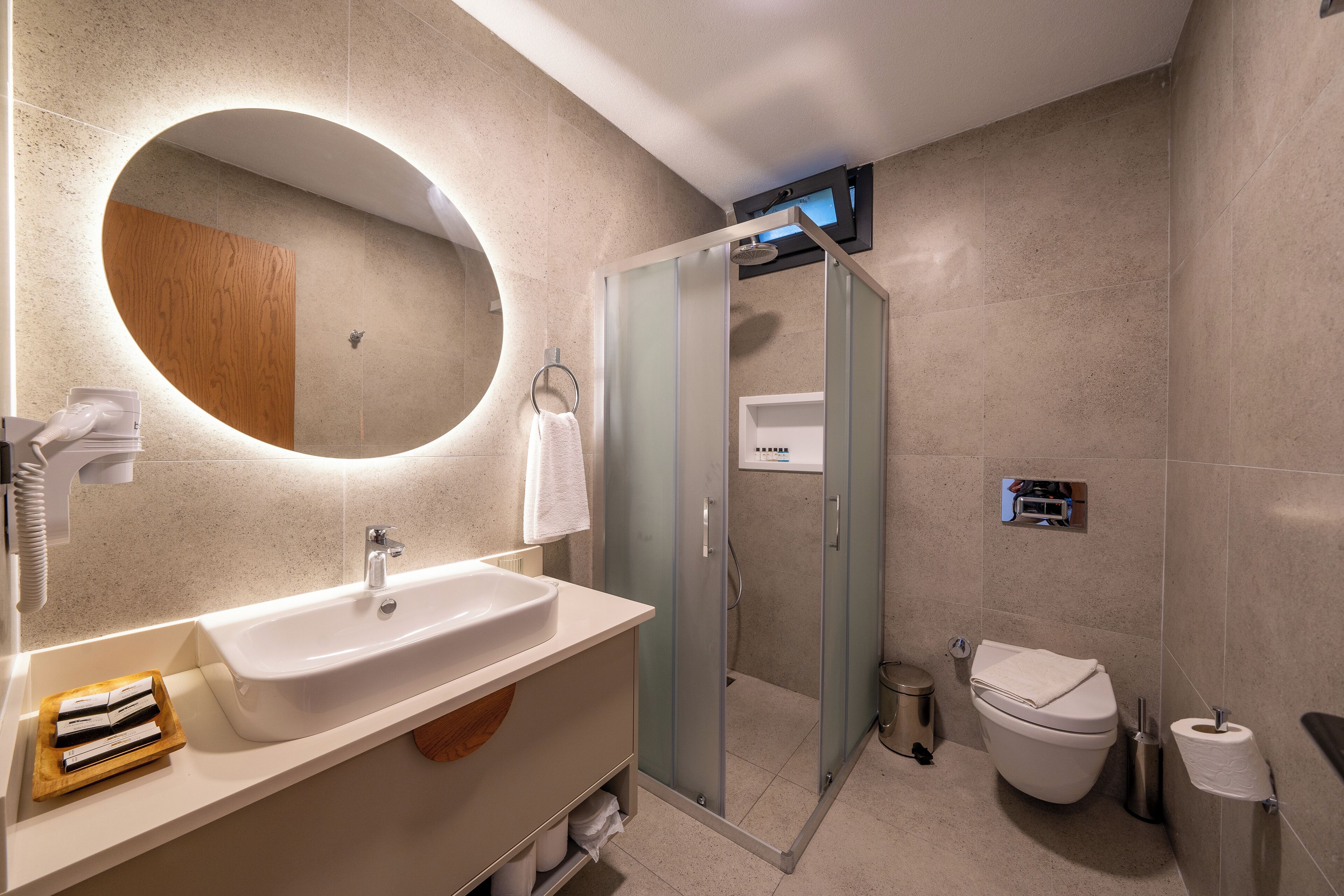 Une salle de bain moderne avec un grand miroir ovale, un lavabo blanc, une douche à parois de verre et des toilettes.