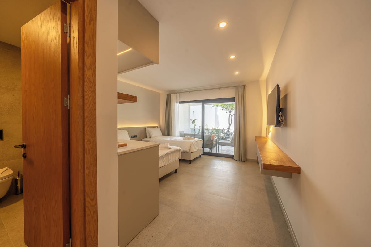 A hotel room with a wooden door, a bed, a desk, and a balcony with a view.