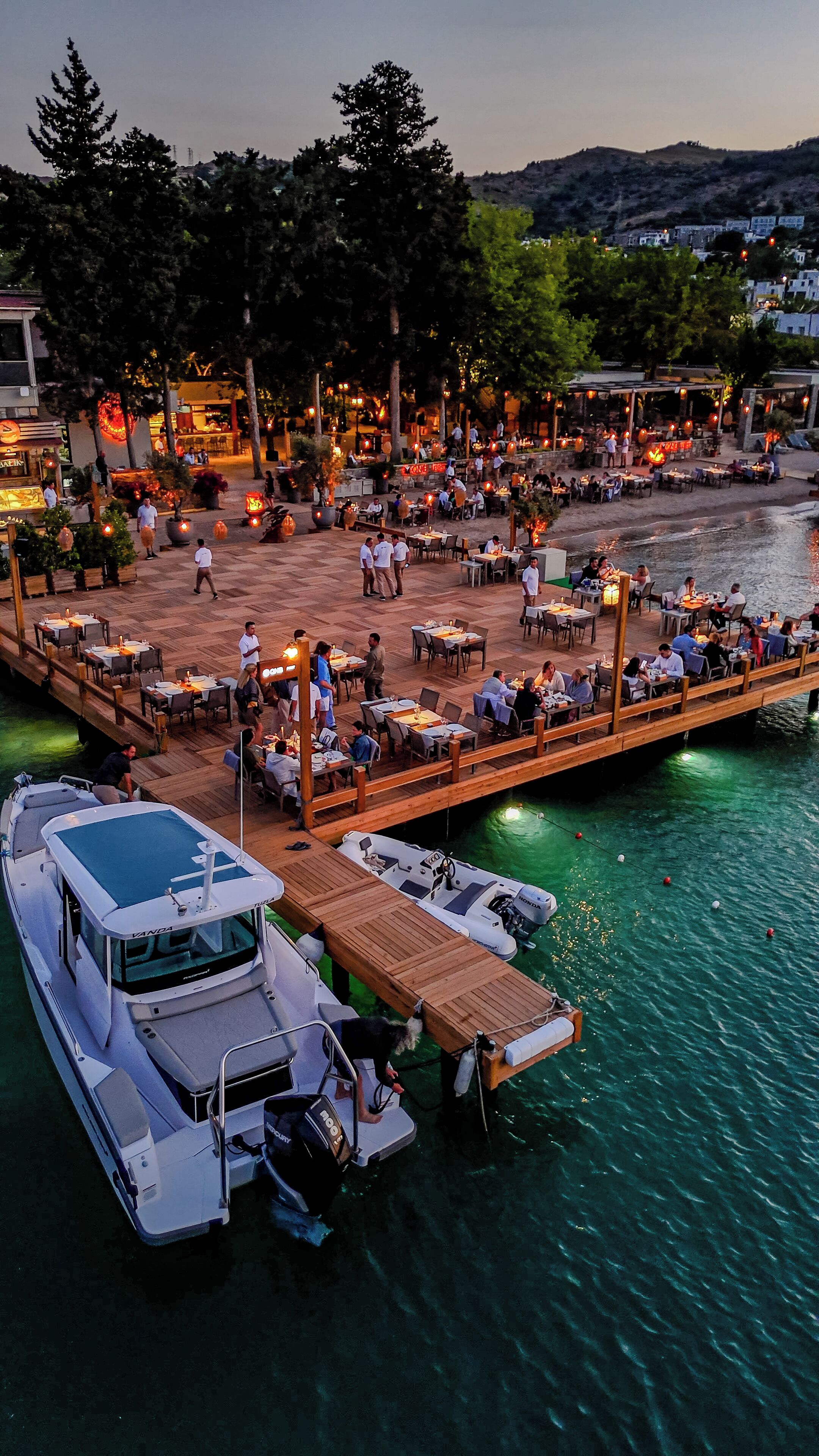 A waterfront restaurant with outdoor seating, boats docked, and a wooden deck.