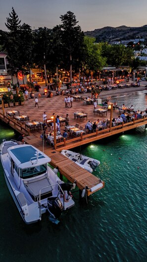 A waterfront restaurant with outdoor seating, boats docked, and a wooden deck. - Orkide Bodrum (Bodrum)