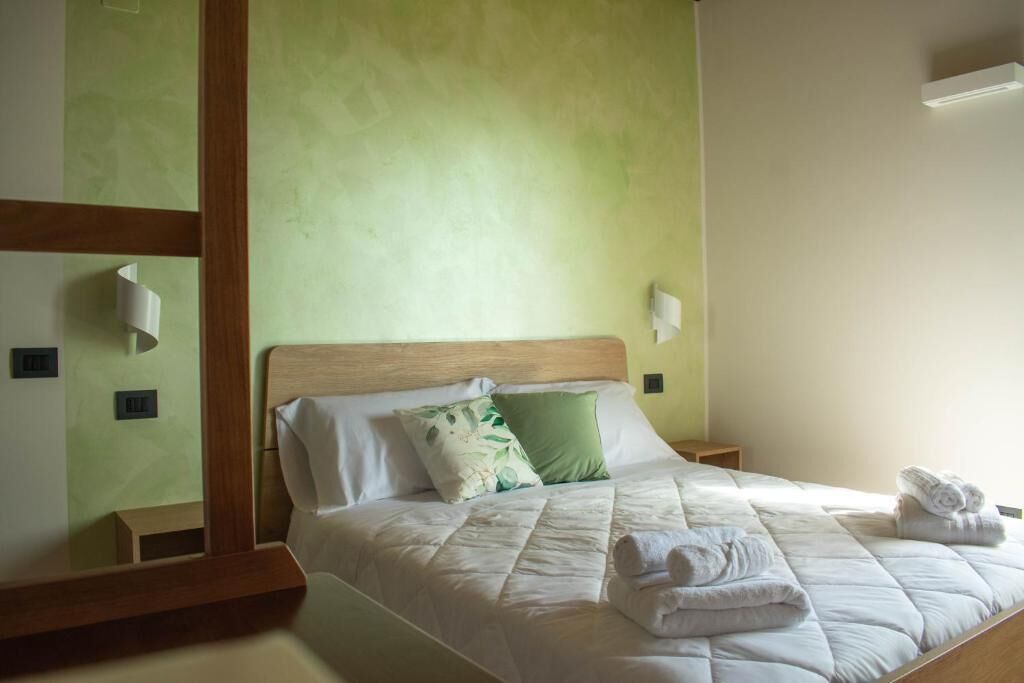 Un letto ben rifatto con biancheria bianca e cuscini verdi, una testiera in legno e un comodino con una lampada.